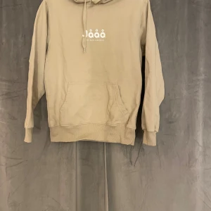 Beige hoodie från Emil Hansius - Säljer en beige hoodie från Emil Hansius med trycket 'Jååå' på bröstet. Hoodien har huva med snörning, magficka och ribbade muddar. Perfekt för chill dagar och enkel att matcha med jeans eller mjukisbyxor. aldrig använd!