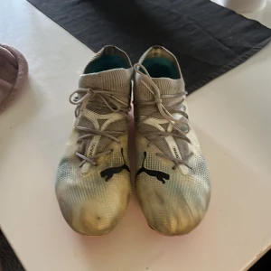 Puma grå fotbollsskor med snörning - Snygga grå fotbollsskor från Puma med svart logga på ovansidan och coola detaljer på sidorna. Skorna har snörning och en stickad, strumpliknande krage för extra komfort. Yttersulan är i en kontrasterande röd färg och ovandelen är i syntetmaterial.