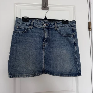 Blå jeanskjol med fickor - Snygg blå jeanskjol i klassisk modell med fem fickor, bälteshällor och knappstängning fram. Kjolen är kort och har en rak passform, perfekt till sneakers eller boots. Tidlös denim-look som funkar året runt.