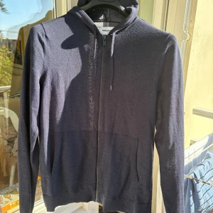 Mörkblå hoodie från Zadig & Voltaire - Snygg mörkblå hoodie från Zadig & Voltaire i merinoull och polyester. Tröjan har huva med snörning, dragkedja framtill och två fickor. Perfekt för dig som gillar stilrena och bekväma plagg med premiumkänsla.