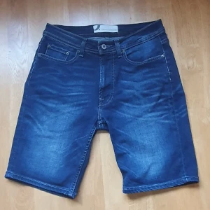 Mörkblå jeansshorts Dressmann i bomull S - Snygga mörkblå Dressmann jeansshorts med klassisk femficksdesign och dragkedjestängning. Tillverkade i mjuk bomull med lite stretch för skön passform. Perfekt längd som slutar strax ovanför knäna och passar till chillade dagar. Tidlös stil och slitningar för extra edge. 