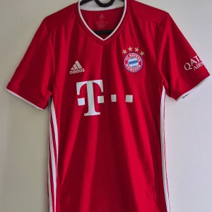Bayern München 20/21 hemmatröja  - Riktigt snygg FC Bayern München hemmatröja från Adidas i röd färg med vita detaljer och broderat klubbmärke på bröstet. Tröjan har korta ärmar, V-ringad krage och är gjord i lätt, ventilerande Aeroready-material. Perfekt för dig som vill representera Bayern.