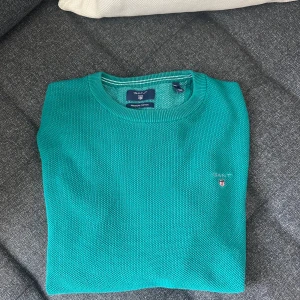 Turkos bomullströja från GANT - Snygg turkos tröja från GANT i bomull med diskret strukturstickning. Klassisk rund halsringning och broderad GANT-logga på bröstet. Långärmad modell med ribbade muddar och avslut. Tröjan är i nyskick och har använts sparsamt.