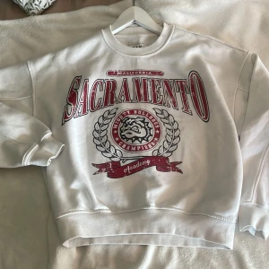 Vit sweatshirt med tryck - Vit oversized sweatshirt med stort rött och svart tryck.  Perfekt för en chill och sportig look.
