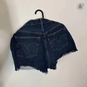 Levi's Premium mörkblå jeansshorts - Snygga mörkblå jeansshorts från Levi's Premium med fransig kant och klassiska fem fickor. Shortsen har hög midja och slitna detaljer framtill för en cool vibe. Perfekta för sommaren och passar till allt. Ikonisk Levi's-label på baksidan.