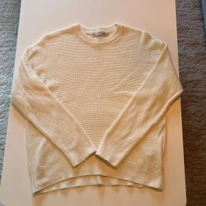 Vit stickad tröja från 157 - Säljer en vit stickad tröja från 157 med långärmad design och ribbade muddar. Tröjan har en snygg, diskret struktur och rund halsringning. Perfekt för dig som gillar enkel och stilren look.