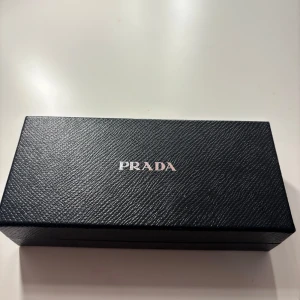 PRADA solglasögon - Snygga solglasögon från Prada med brunmelerad båge och svarta detaljer. Modellen har en klassisk rundad form och loggan i guld på sidan. Kommer med originaletui och ask. Perfekt accessoar för dig som vill ha en lyxig vibe.💞💞