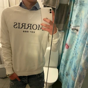Vit Morris sweater - Säljer en riktigt snygg vit sweatshirt från Morris med trycket ”MORRIS EST 1968” på framsidan. Tröjan har rund halsringning perfekt att bära över en skjorta för en stilren look.