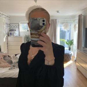 Svart blus med spets och puffärm - Säljer en svart blus med djup v-ringning och spetsdetaljer längs halsen. Blusen har puffiga långärmar med resår vid ärmslut och en flowy passform. Perfekt för dig som gillar en stilren look med lite extra edge.