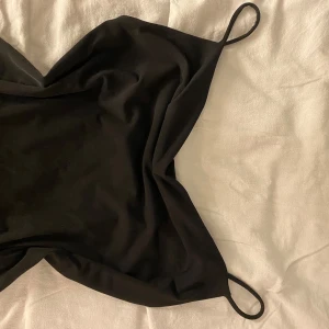 Svart linnetopp från Gina Tricot - Säljer en svart linnetopp från Gina Tricot i storlek XXS. Toppen har tunna axelband och en enkel, stilren design som är lätt att matcha. Materialet känns mjukt och följsamt, perfekt för en clean och snygg look.