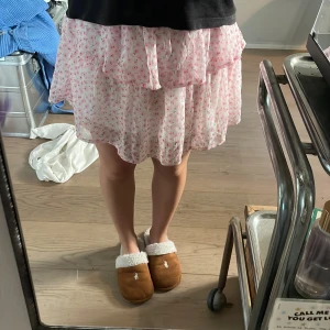 Rosa blommig volangkjol Vero Moda - Supersöt kort kjol från Vero Moda med volanger och töjbar midja. Kjolen är vit med små rosa blommor och har en luftig, flowy känsla.