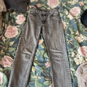 Grå jeans från Nudie Jeans, stl 28/30 - Snygga grå jeans från Nudie Jeans med klassisk femficksmodell och svarta detaljer på bakfickorna. Jeansen har rak passform och är tillverkade i slitstarkt bomullstyg. Perfekta för dig som gillar en clean och tidlös look.