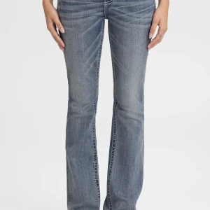 Blå bootcut jeans med kontrastsömmar - Snygga blå bootcut jeans med ljus tvätt och markerade kontrastsömmar. Jeansen har dekorativa fickor med detaljerade sömmar och silverfärgade nitar. Klassisk femficksmodell i mjukt denimtyg som sitter skönt på kroppen. Det är samma byxor men det vita märket är svart på dem jag har💕