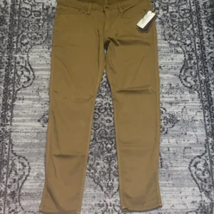  DU/ER Pants - Snabb leverans! Aldrig använda helt ny med tag! Snygga bruna byxor från DU/ER med fem fickor och raka ben. Tillverkade i ett tekniskt material som känns mjukt och följsamt. Klassisk design med bälteshällor och knappstängning. Perfekta för dig som vill ha både stil och komfort.