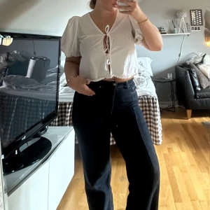 Vit croppad blus med snörning - Supersöt vit blus med puffärmar och croppad passform. Framtill finns en snygg snörningsdetalj som ger en trendig look. Perfekt till höga jeans eller kjol. Tunn och luftig i bomull, perfekt för varmare dagar.