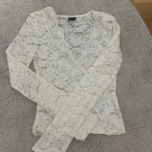 Vit spetsblus från Gina Tricot - Superfin vit blus i spets från Gina Tricot med lång ärm och v-ringning. Blusen har ett blommigt spetsmönster och är genomskinlig, perfekt att styla med ett linne under. Helt oanvänd. Snygg passform och mjukt material. Köptes för 350kr och säljs för 299kr 