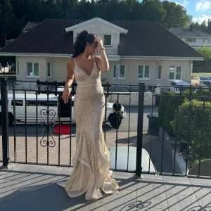 Champagnefärgad glittrig långklänning - Säljer en elegant champagnefärgad långklänning med glittriga paljetter och v-ringad front. Klänningen har smala axelband, figurnära passform och en dramatisk volangdetalj vid nederdelen. Perfekt för bal eller fest, ger en lyxig och glamorös känsla. Använd endast en gång ✨