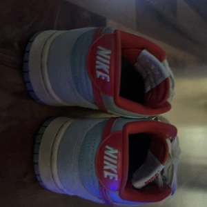 Nike sneakers Athletic Dept vit/röd - Nike sneakers Athletic Dept med vit ovandel i skinn och röda detaljer på swoosh, häl och foder. Klassisk låg modell med snörning och perforerad tå. Snygg retrostil med beige sula och Athletic Dept-tryck i innersulan. Behöver bara tvätta så e dom som nya igen