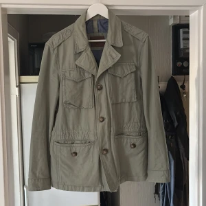  Jacka Massimo Dutti - Stilren grön jacka från Massimo Dutti med fyra fickor framtill och snygga knappar. Jackan har klassisk krage, axelklaffar och detaljerad sömnad. Perfekt för dig som vill ha en clean och tidlös look.