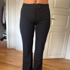 Svarta bootcut kostymbyxor med hög midja - Snygga svarta kostymbyxor med bootcut och hög midja. De har en stilren look med slät framsida och lätt stretchigt material som sitter bekvämt. Perfekta för dig som gillar en klassisk men trendig siluett.