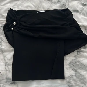 Svart ribbad topp från Zara XS - Supersnygg svart ribbad topp från Zara i storlek XS. Off shoulder-modell med cool drapering och stora pärldetaljer framtill. Stretchigt material som sitter tajt och markerar midjan. Perfekt för dig som vill sticka ut med en trendig och elegant look. Pris kan diskuteras 