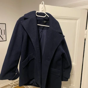 Mörkblå skepparkavaj från Gina Tricot - Säljer en snygg mörkblå kappa från Gina Tricot med klassisk krage och två stora fickor framtill. Jackan är i ullmaterial och har en loose passform med långa ärmar. Perfekt för dig som gillar stilrena och tidlösa plagg. Har används ett par gånger men ser ut som ny. Köpte för 900kr
