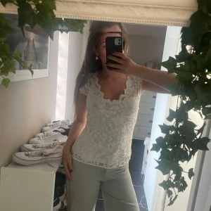Vit spetsblus med v-ringning Gina  - Säljer en vit blus i spets med v-ringad hals och korta ärmar. Blusen har ett blommigt spetsmönster och sitter figurnära. Perfekt för dig som gillar romantisk och feminin stil. Superfin att matcha med jeans eller kjol!