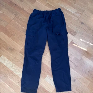 Svarta cargopants från SOC - Svarta cargopants från SOC med elastisk midja och snörning. Byxorna har flera praktiska fickor på sidorna och är tillverkade i ett lätt och syntetiskt material. Pris kan diskuteras. 