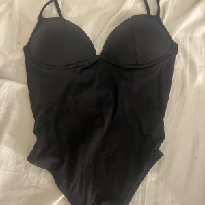 Svart body  - Snygg svart body med vadderade kupor och justerbara axelband. Klassisk och stilren modell som ger bra stöd och passar perfekt till fest. Mjukt material som känns skönt mot huden.