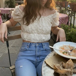 Offshoulder spetstopp  - Romantisk offshoulder topp i ljusbeige spets med broderade blommor. Jag vet tyvärr inte storleken men skulle gissa på storlek Xs