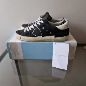 Philippe model skor  - Svarta Philippe Model sneakers i mocka med vita detaljer och snörning. Skorna har vit sula och vit hälkappa med logotyp, samt rund tå och platt sula. Klassisk och stilren design som passar till det mesta.