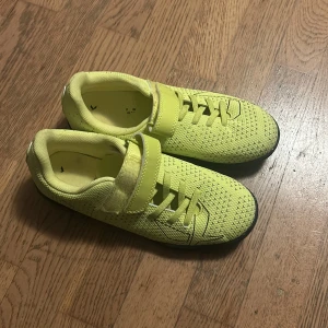 Gula gröna fotbollsskor med kardborre - Säljer ett par gula gröna fotbollsskor med svart sula och snyggt mönstrad ovandel. Skorna har både snörning och kardborreband för extra bra passform. Ovandelen är i syntetmaterial som andas och sulan är platt med bra grepp. Perfekta för inomhusspel! Pris kan sänkas !!!!!