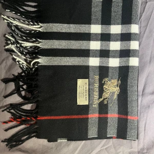 Halsduk från Burberry - Snygg halsduk från Burberry i klassiskt rutigt mönster med svarta, vita och röda detaljer. Halsduken är tillverkad i 100% kashmir och har broderad Burberry-logga samt fransar i ändarna. Perfekt accessoar för att lyfta din outfit.