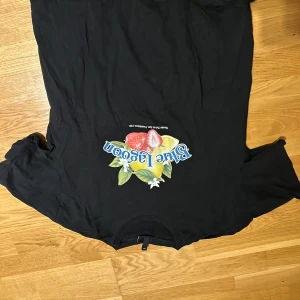 Svart Blue Lagoon t-shirt med tryck - Svart t-shirt från H&M med färgglatt Blue Lagoon-tryck framtill som visar citron, jordgubbe och blommor. Klassisk rund hals och korta ärmar. Perfekt för dig som gillar coola prints och vill sticka ut lite extra.