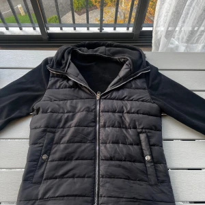 Svart cardigan ifrån H&M - Svart pufferjacka från H&M i storlek S. Jackan har quiltad framsida, släta ärmar och rygg, samt praktisk huva. Stängs med dragkedja och har två fickor med knapp framtill. Perfekt för kyliga dagar och enkel att matcha med allt.