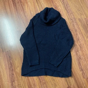 Mörkblå stickad polotröja - Mysig mörkblå stickad polotröja med grov struktur och hög, bred polokrage. Tröjan har lång ärm och något längre bakstycke för en chill look. Perfekt för kalla dagar när du vill vara både varm och snygg.