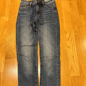 Crocker blå jeans high waist 24/28 - Blå jeans från Crocker med snyggt slitna detaljer och klassisk femficksmodell. Modellen är high waist och har raka ben. Jeansen är i denim med kontrastsömmar och har läderpatch bak i midjan.