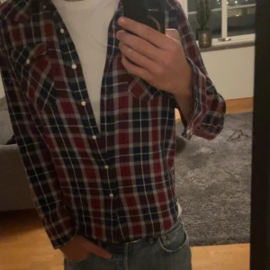 Rutig Levi's skjorta i blått och rött - Säljer en snygg rutig skjorta från Levi's i blått, rött och vitt. Skjortan har lång ärm, klassisk krage och vita knappar framtill. Två bröstfickor med knappstängning ger extra stilpoäng. Perfekt att bära öppen över en t-shirt eller knäppt.