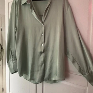 Ljusgrön skjorta med knappar - Snygg ljusgrön skjorta med klassisk krage och knappar framtill. Skjortan har lång ärm med knapp vid manschetten och är tillverkad i ett mjukt, tunt material som ger en skön känsla. Perfekt för dig som gillar stilrena och enkla plagg.