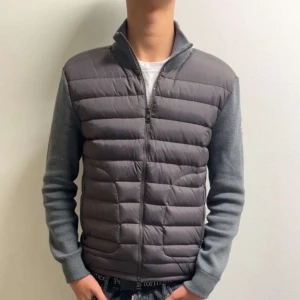 Moncler cardigan - Snygg grå dunjacka från Moncler med quiltad front och stickade ärmar. Jackan har dragkedja hela vägen, ståkrage och Moncler-logga på ärmen. Perfekt för dig som gillar stilren design och vill ha något som håller värmen under kyliga dagar. Den är i storlek M och den är i mycket bra skick har använt några gånger bara.