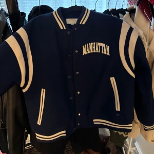 Blå bomberjacka Manhattan Pull&Bear - Säljer en blå bomberjacka från Pull&Bear med vita detaljer och Manhattan-tryck fram och bak. Jackan har ribbade muddar, tryckknappar och två fickor. Perfekt för dig som vill ha en sportig och cool look. Hör av er för mer bilder eller frågor!☺️