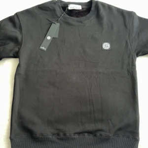 Svart sweatshirt från Stone Island - Svart sweatshirt från Stone Island med klassisk rund hals och ribbade muddar. Tröjan har en snygg broderad logotyp på bröstet och är tillverkad i mjuk bomull. Perfekt för dig som gillar  stilrena och enkla plagg med streetkäns. Storlek M men kan säga S är passar bättre/ tröjan har skit varmt och mjukt inne i tröjan.