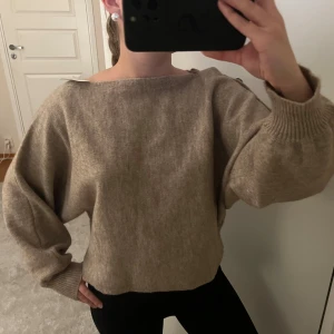 Beige stickad tröja med knappar - Beige stickad tröja med oversized passform och bred halsringning. Tröjan har långa ärmar med ribbade muddar och snygga knappdetaljer på axlarna. Perfekt för lager-på-lager och chill stil.