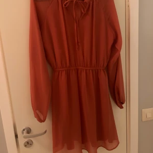 Rosa kort klänning DeFacto - Snygg rosa klänning från DeFacto med långa ärmar och transparenta detaljer vid axlarna. Klänningen har ett knytband vid halsen och ett elastiskt midjeparti som ger en fin siluett. 