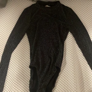 Glittrig svart långärmad bodysuit H&M - Säljer en svart glittrig bodysuit från H&M Divided i storlek S. Öppen rygg väldigt fin till jeans, tjol och mjukis. Köpter för 600kr men säljs för 200 knappt använd i nästan nytt skick