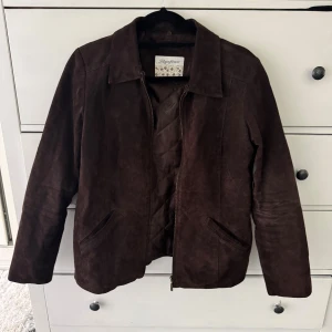 Brun mockajacka från Rainforest - Snygg brun mockajacka från Rainforest i klassisk modell med krage och dragkedja framtill. Jackan har två sneda fickor och är helfärgad utan mönster. Perfekt för dig som gillar stilren och tidlös look.