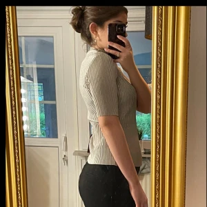 Ribbad beige topp med halvpolo - Säljer en ribbad topp i beige med smal passform och halvpolo. Toppen har korta ärmar och ett stilrent, randigt mönster i strukturen. 