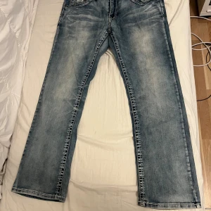 Blå jeans från SMOG Denim Classics - Snygga blå jeans från SMOG Denim Classics med klassisk tvättad look och kontrastsömmar. Modellen har raka ben och fem fickor, samt coola detaljer på bakfickorna. Perfekt för dig som gillar en avslappnad och tidlös stil.
