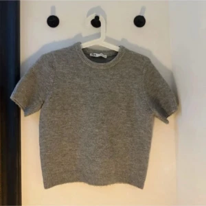 Grå stickad kortärmad tröja Zara - Grå stickad tröja från Zara med korta ärmar och rund halsringning. Tröjan har en enkel och clean look med ribbade muddar vid ärmslut och nederkant. 