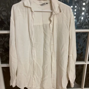 Vit linneskjorta - Klassisk vit skjorta i linne. Skjortan har lång ärm, knappar hela vägen och en avslappnad krage. Perfekt för en clean och stilren look, lätt att matcha med jeans eller shorts. Köpt från stradivarius. 